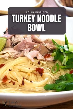 a white bowl filled with noodles, meat and garnishes on top of a wooden table