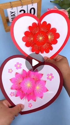 someone is holding up two heart shaped cards with flowers on the front and bottom, while another