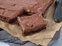 two pieces of chocolate cake sitting on top of brown paper next to a spatula