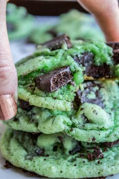 a close up of a person holding a chocolate chip cookie in front of green cookies