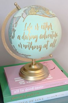 a globe with writing on it sitting on top of two pink and green books in front of a white wall