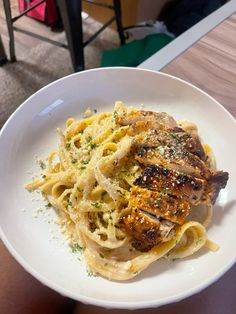 a white plate topped with pasta and meat covered in parmesan cheese on top of a wooden table