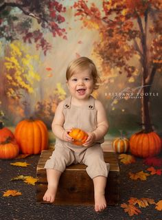 a baby is sitting on a crate with pumpkins in front of her and smiling