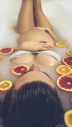 a woman laying in a bath filled with oranges and blood orange slices on the floor