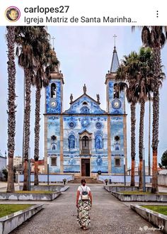 a person walking down a street in front of a blue church with palm trees on either side