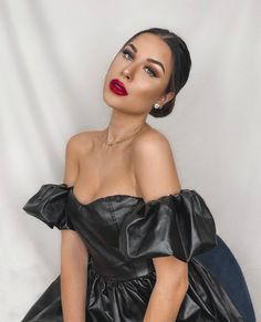 a woman wearing a black dress and red lipstick sitting on a blue chair in front of a white backdrop