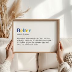 a person holding up a framed poster with the words better on it in front of a white couch