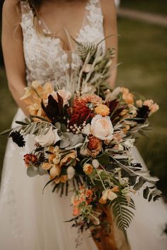 a woman in a wedding dress holding a large bouquet with flowers and foliage on it