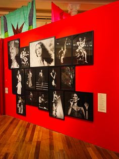 a red wall with many black and white photos on it, along with wooden flooring