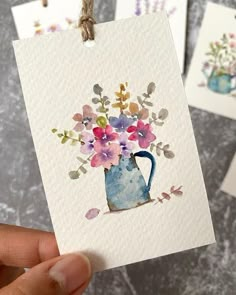 three cards with watercolor flowers on them are being held by someone's hand