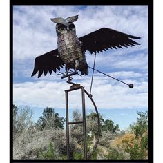 an owl sculpture on top of a metal stand in the middle of a grassy area