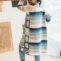 a woman standing in front of a window wearing a crocheted sweater and jeans