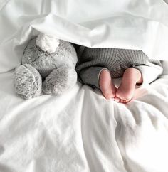 a baby laying in bed under a blanket with a stuffed animal on it's side