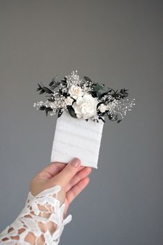 a hand holding a white box with flowers in it and lace on the sleeves,