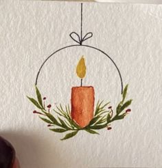 a drawing of a candle in a circle with greenery around it and a hand holding a pen