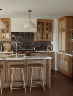 a large kitchen with wooden cabinets and marble counter tops, along with two bar stools