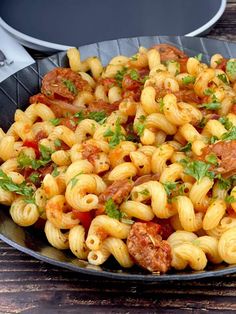 a skillet filled with pasta and sauce on top of a wooden table