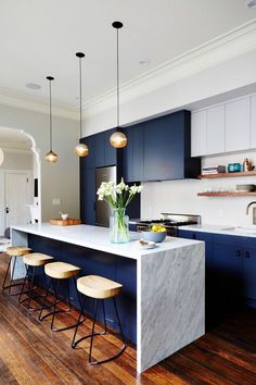 a kitchen with blue cabinets and marble counter tops, stools at the center island