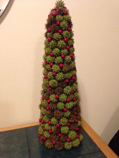 a christmas tree made out of pine cones and red berries is on a table next to a clock