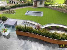 an aerial view of a backyard with grass and flowers in the center, surrounded by landscaping