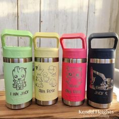 four different colored insulated water bottles sitting on top of a wooden table next to each other