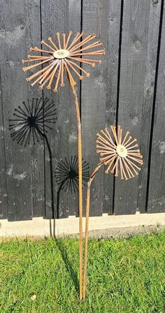 two metal flowers sitting in the grass next to a fence