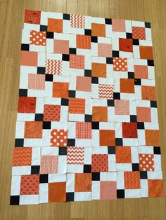 an orange and black patchwork quilt sitting on top of a wooden floor