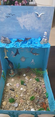 an open cardboard box filled with sea animals and rocks on top of a wooden table