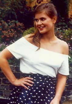 a woman standing in front of a brick wall wearing a white top and black polka dot skirt