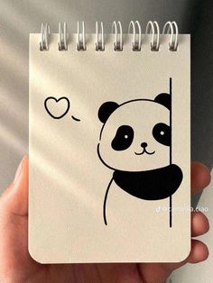 a hand holding a spiral notebook with a panda face on it and a heart drawn on the cover