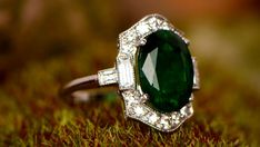 an emerald and diamond ring sits on moss