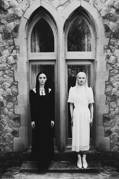 two women standing in front of an old stone building with double doors and arched windows