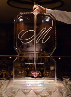 a person pouring wine into glasses in front of a sign with the letter e on it