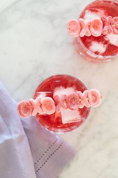 two glasses filled with ice and pink flowers on top of a white marble countertop