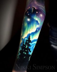 a man's arm with an aurora bore tattoo on it and trees in the foreground