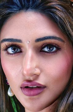 a close up of a woman with blue eyes and piercings on her nose, looking at the camera