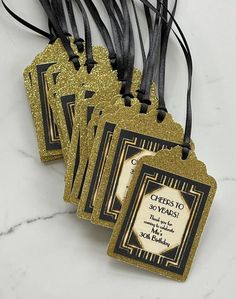 four tags with black and gold designs are on a marble countertop in front of a white background