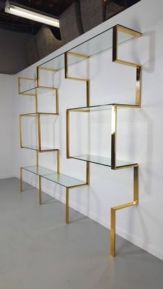 a shelf that has some glass shelves on it and gold trim around the edges, in front of a white wall