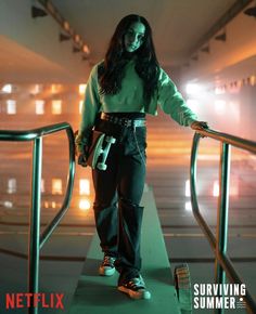 a woman in green shirt and black pants standing on metal handrail with her arms outstretched