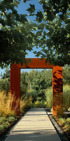 an orange arch is in the middle of a walkway surrounded by grass and trees on both sides