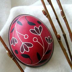 a red painted egg sitting on top of a white cloth next to some brown branches