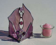 a pink candle holder next to a glass container with a candle in it on a white surface