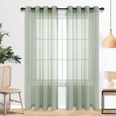 a living room with white walls and green curtains on the windowsills, a wicker chair and potted plant