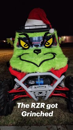 a green and red monster truck with santa hat on it's head in the grass