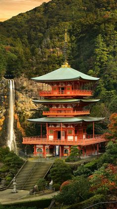 a tall red building sitting on top of a lush green hillside next to a waterfall