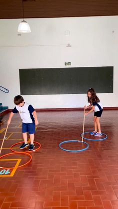 two young children playing with colored circles in an indoor gym area, one boy is holding a stick and the other girl is standing behind him