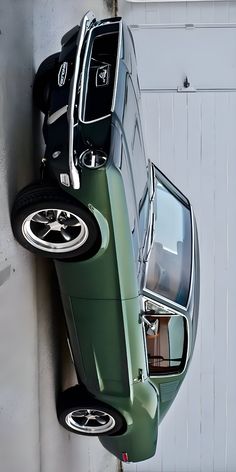 a green car parked next to a white wall