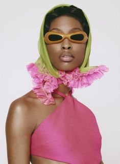 a woman wearing sunglasses and a pink dress with flowers on her neck, standing in front of a white background