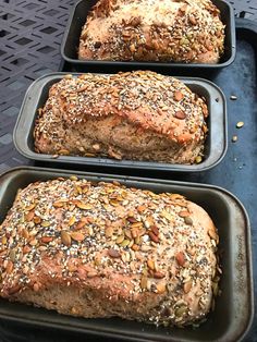 three loafs of bread sitting on top of pans covered in sesame seed sprinkles