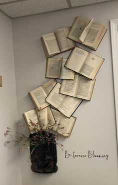 an arrangement of open books on the wall above a vase with pink flowers in it